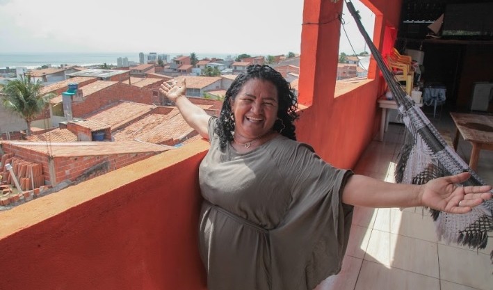 mulher posa na varanda de casa tendo como pano de fundo o litoral de Fortaleza